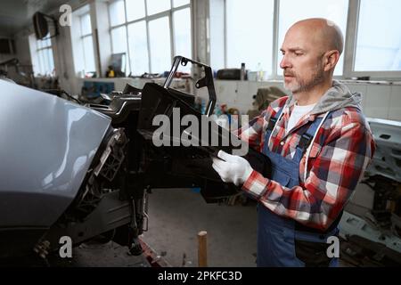 Der Mann in der Autoherstellung zerlegt ein kaputtes Auto für Teile Stockfoto