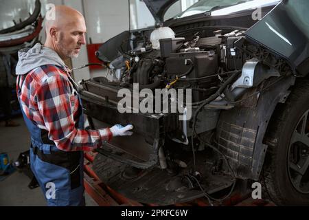 Glatzkopf-Meister ersetzt Stoßfänger in einer Autowerkstatt Stockfoto