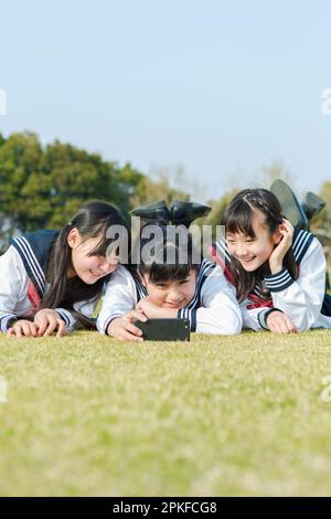 Ein Schulmädchen, das auf dem Rasen liegt und ein Foto macht Stockfoto