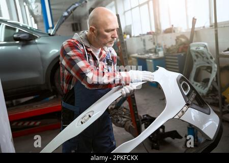 Mitarbeiter einer Autowerkstatt untersucht einen Teil der Fahrzeugkarosserie Stockfoto