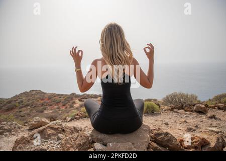 Ein Wanderer übt Yoga-Übungen, um sich auf einem Felsen auf dem Gipfel des Berges zu entspannen Stockfoto