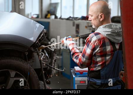 Ein erfahrener Techniker setzt einen Spotter ein, um ein Fahrzeug zu reparieren Stockfoto