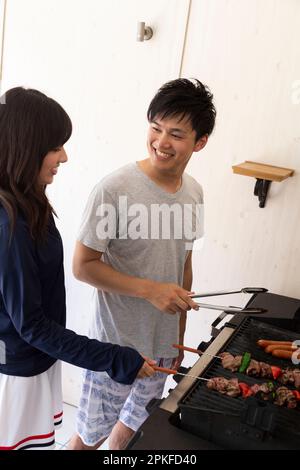 Ein junges Paar grillt Fleisch auf dem Grill Stockfoto