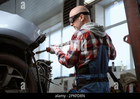 Autowerkstatt in Schutzbrille arbeitet als Spotter für die Fahrzeugreparatur Stockfoto