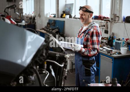 Zufriedener Mann steht in der Werkstatt mit Arbeitsunterlagen in der Hand Stockfoto