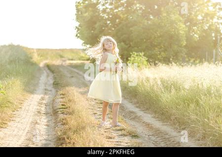 Bezauberndes Mädchen mit langen blonden Haaren auf dem Landweg in Sommeratmosphäre Stockfoto