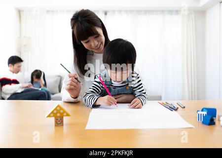 Mutter und Sohn zeichnen ein Bild und Vater und Tochter lesen ein Bilderbuch Stockfoto