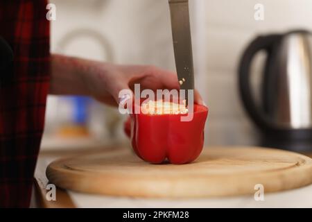 Eine Frau schneidet rote Paprika auf einem Holzbrett. Weibliche Person, die einen Salat mit frischem Gemüse kocht Stockfoto