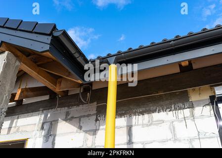 Gelbes PVC-Rohr mit einem Durchmesser von 100mm mm, das mit dem Ende der Dachrinne verbunden und gegen Wasser geschützt ist. Stockfoto