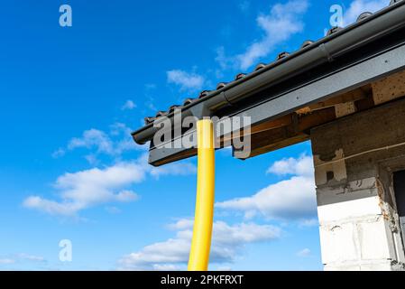 Gelbes PVC-Rohr mit einem Durchmesser von 100mm mm, das mit dem Ende der Dachrinne verbunden und gegen Wasser geschützt ist. Stockfoto