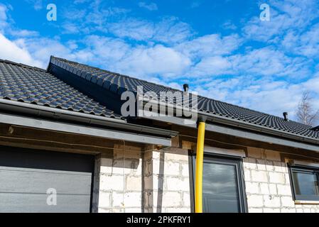 Gelbes PVC-Rohr mit einem Durchmesser von 100mm mm, das mit dem Ende der Dachrinne verbunden und gegen Wasser geschützt ist. Stockfoto