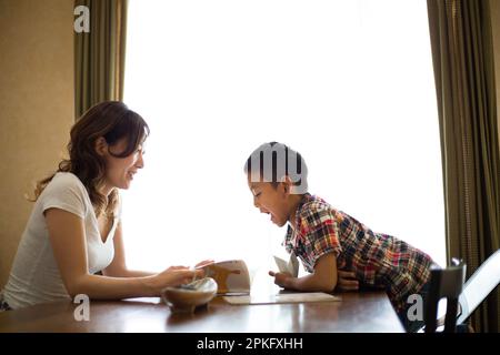 Einem Grundschuljungen wird das Lernen von seiner Mutter im Wohnzimmer beigebracht Stockfoto