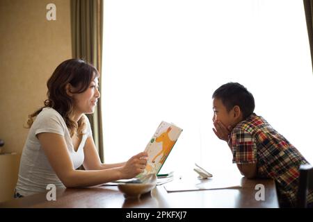 Einem Grundschuljungen wird das Lernen von seiner Mutter im Wohnzimmer beigebracht Stockfoto