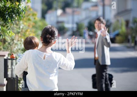 Frau mit Baby winkt dem Ehemann auf dem Weg zur Arbeit zu Stockfoto