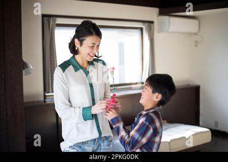 Der Junge aus der Grundschule schenkt seiner Mutter eine Nelke Stockfoto