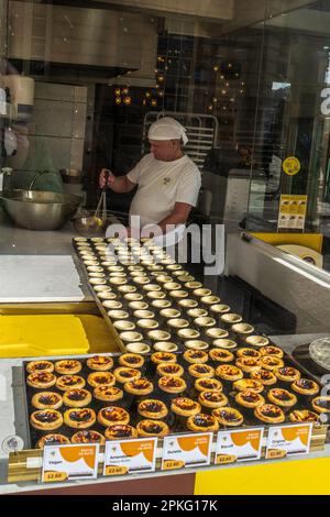 Sehen Sie durch das Fenster eines Bäckers, der Pasteis de Nata oder portugiesische Vanilletörtchen in einer handwerklichen Bäckerei in Bath, England, herstellt Stockfoto