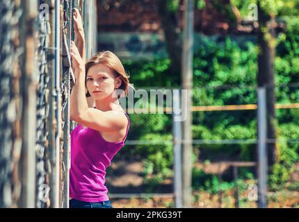 Junge Frau an einem Metallzaun auf einem Sportplatz Stockfoto