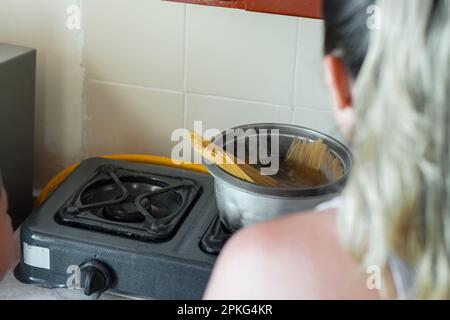 Nahaufnahme einer jungen Frau, die die Spaghetti im Topf kochen sieht Stockfoto