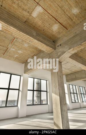 Ein leerer Raum mit Holzbalken an der Decke und Fenstern auf dem Foto wird von innen mit Blick nach draußen aufgenommen Stockfoto