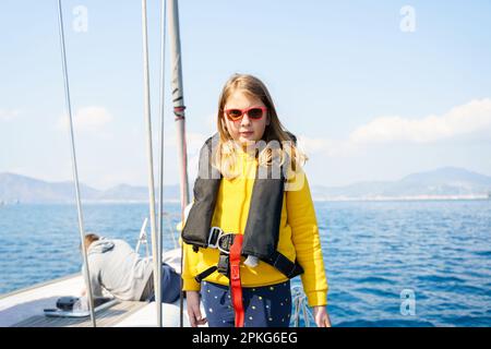 Fahrt Segeltörn auf einer luxuriösen Sportyacht. Bootsfahrt mit der Familie im Sommer. Kinder, Matrosenjunge, die in einer kleinen Rettungsweste segelt. Ozean-Shi Stockfoto