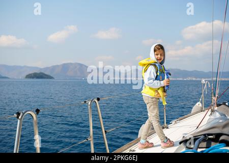 Fahrt Segeltörn auf einer luxuriösen Sportyacht. Bootsfahrt mit der Familie im Sommer. Kinder, Matrosenjunge, die in einer kleinen Rettungsweste segelt. Ozean-Shi Stockfoto