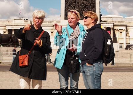 Drei Frauen, Freunde, die vor Nelsons Kolumne stehen, Trafalgar Square, London. Großbritannien zeigt auf, wie es weitergeht Stockfoto