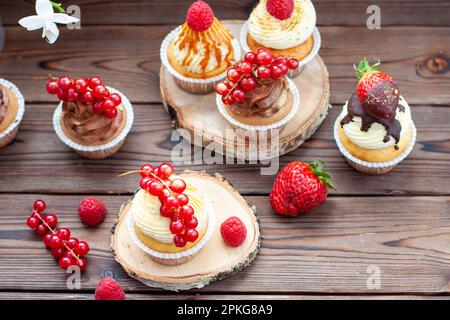 Schokoladen- und Vanille-Cupcakes mit frischen Beeren auf rustikalem Holzhintergrund Stockfoto