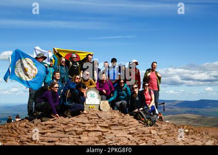 UK Weather: Karfreitag-Feiertag, 7. April 2023. Brecon Beacons National Park, Südwales. Eine Gruppe Wanderer aus Manchester mit den Flaggen Lancashire und Yorkshire lassen sich am Trig Point auf dem Gipfel des Pen y Fan im Brecon Beacons National Park fotografieren. Pen y Fan (886m / 2.907ft) ist der höchste Gipfel im Brecon Beacons National Park und im Süden Großbritanniens und ein beliebtes Wanderziel. Das schöne, sonnige Wetter bedeutete, dass viele Leute die Reise in den Park für den heutigen Feiertag machten. Stockfoto