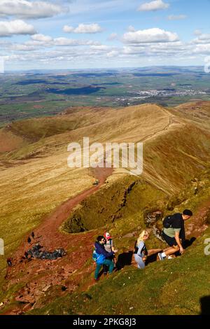 UK Weather: Karfreitag-Feiertag, 7. April 2023. Brecon Beacons National Park, Südwales. Wanderer auf dem Pfad vom Norden entlang Cefn Cwm Llwch zum Pen y Fan Mountain erklimmen den letzten steilen Aufstieg zum Gipfel. Pen y Fan (886m / 2.907ft) ist der höchste Gipfel im Brecon Beacons National Park und im Süden Großbritanniens und ein beliebtes Wanderziel. Die Stadt Brecon ist in der Ferne. Das schöne, sonnige Wetter bedeutete, dass viele Leute die Reise in den Park für den heutigen Feiertag machten. Stockfoto