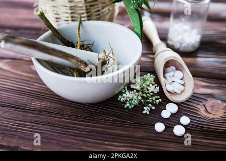 Valerian-Tabletten mit sedierenden Eigenschaften. Pharmazeutischer Becher mit Pillen auf einem Holztisch. Baldrianwurzel in einem Mörser für Herbalismus-Elixier kochen Stockfoto