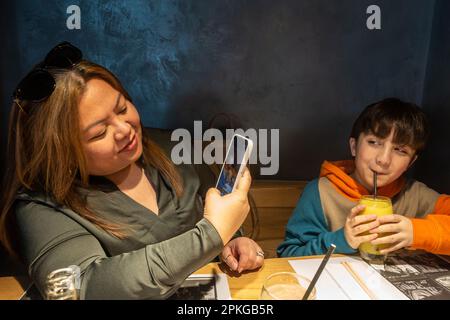 Eine Mutter macht ein Foto ihres Sohnes mit ihrem Handy, während sie in einem Restaurant speist Stockfoto