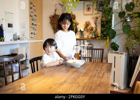 Ältere Schwester trägt Snacks zu jüngerem Bruder Stockfoto