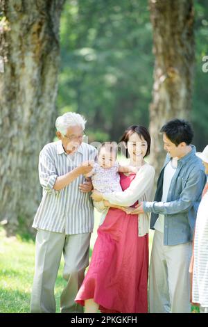 Eine Familie von drei Generationen, die sich an einer Reihe von Pappelbäumen unterhält Stockfoto