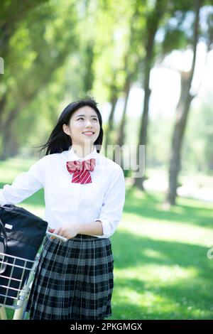 Studentin, die ein Fahrrad auf Pappelbäume schiebt Stockfoto