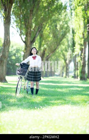Studentin, die ein Fahrrad auf eine Reihe Pappelbäume schiebt Stockfoto