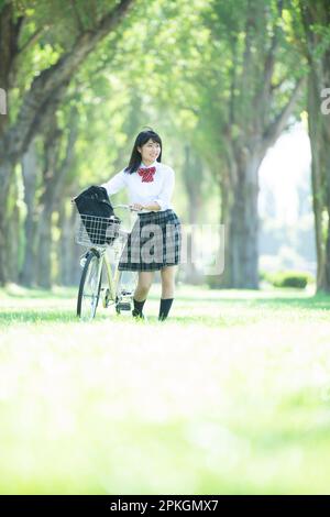 Eine Studentin, die ihr Fahrrad auf eine Reihe Pappelbäume schiebt Stockfoto
