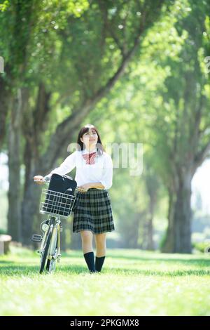 Eine Studentin, die ein Fahrrad entlang von Pappelbäumen schiebt Stockfoto