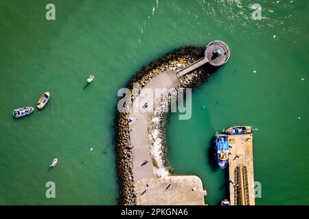 Top-down-Luftaufnahme des Howth Harbor Pier während eines sonnigen Tages mit Menschen, die spazieren gehen und Boote parken Stockfoto