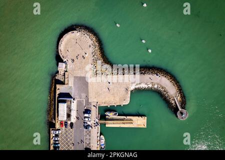 Top-down-Luftaufnahme des Howth Harbor Pier während eines sonnigen Tages mit Menschen, die spazieren gehen und Boote parken Stockfoto