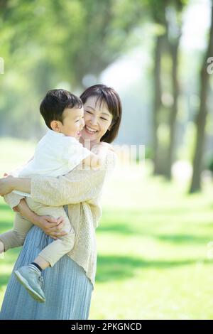 Eine Mutter lächelt, während sie ihr Kind in ihren Armen an einer Reihe von Pappelbäumen hält Stockfoto
