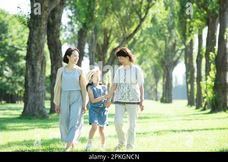 Eine Familie von drei Generationen, die sich an einer Reihe von Pappelbäumen unterhält Stockfoto