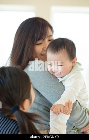 Schwestern, die sich anschauen und lächeln, und Mutter, die zusieht Stockfoto