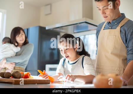 Eine Mutter sieht zu, wie ihre Familie in der Küche kocht Stockfoto