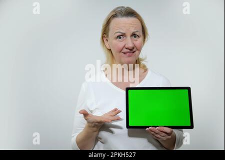 Junge Frau mit negativem Gesichtsausdruck, die ein Chromakey-Board hält und in die Kamera schaut. Chromakey mit Kreuz zur Verfolgung gut geeignet zum Einfügen einiger kommerzieller Bildaufschriften Stockfoto