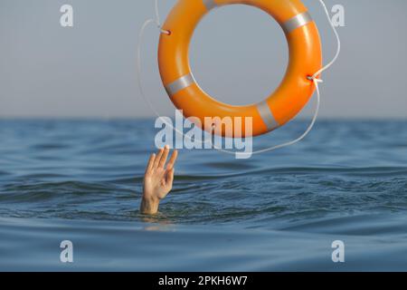 Ertrinkende Frau mit erhobener Hand, die im Meer Rettungsgürtel bekommt Stockfoto