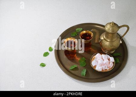 Eine klassische, feierliche, kunstvoll verzierte türkische Teekanne, zwei Gläser und traditionelle türkische Köstlichkeiten auf einem Tablett in sanfter Beleuchtung mit Kopierbereich auf der linken Seite Stockfoto