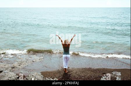 Sie umarmt ihre Tage mit offenen Armen. Rückansicht einer fröhlichen, nicht wiedererkennbaren jungen Frau, die mit weit geöffneten Armen auf den blickt Stockfoto