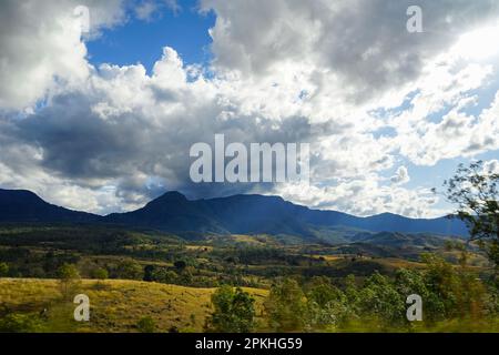 Dramatische dunkle Wolken über entfernten blauen Bergen; Bewegungsunschärfe im Vordergrund; Goldene Hügel, beleuchtet von der Nachmittagssonne. Cunningham Highway Queensland. Stockfoto