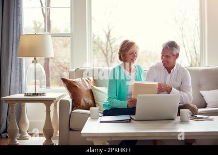 Sieht so aus, als hätten wir diesen Monat mehr gespart als erwartet. Ein reifes Ehepaar, das zu Hause seine Finanzen durchsucht. Stockfoto