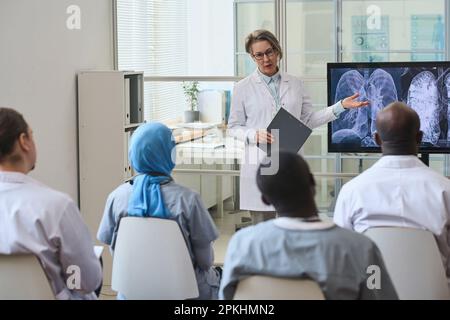 Weibliche Ärztin zeigt auf Monitor mit Röntgenbild der Lunge und diskutiert Krankheit mit ihren Kollegen während der Konferenz Stockfoto